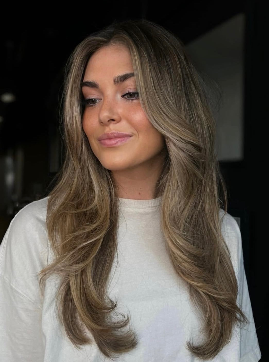 Soft lived-in blonde balayage with seamless root melt and long layered haircut, styled in smooth, voluminous waves for an effortless, dimensional finish.