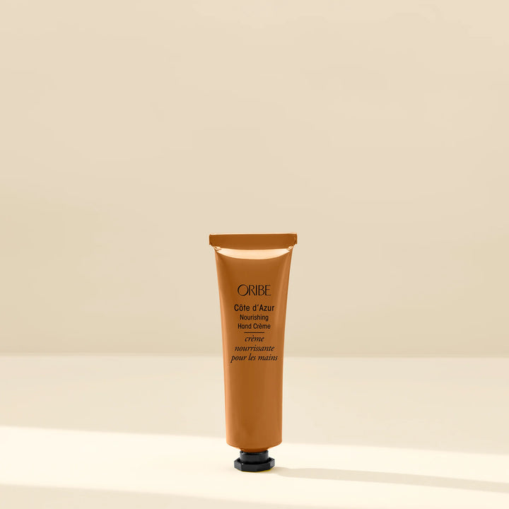 Oribe Côte d’Azur Nourishing Hand Crème travel-size tube on a beige background.