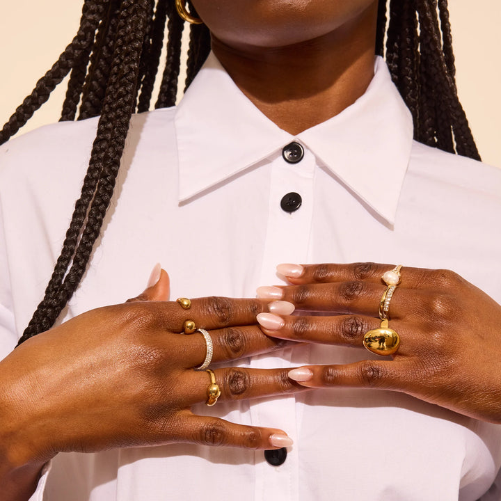 Two hands with nude nails and gold rings, featuring ORIBE Côte d’Azur Nourishing Hand Crème Travel Size