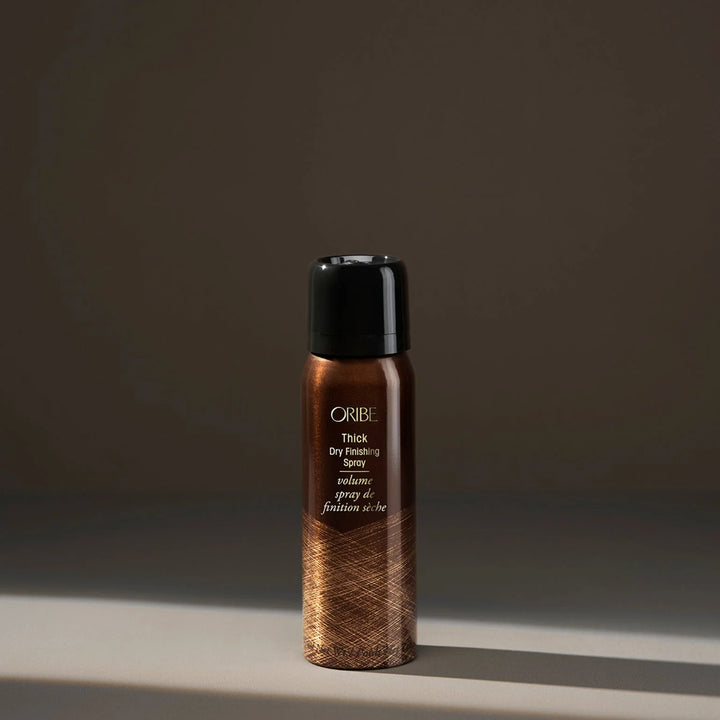 Oribe Thick Dry Finishing Spray bottle on a dark background